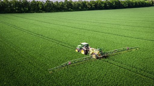 Aerial shot of a tractor spraying fertilizer on an agricultural field.